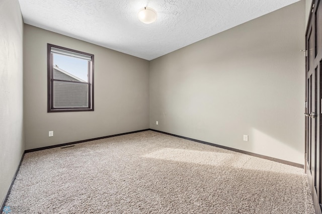 carpeted spare room featuring a textured ceiling and baseboards