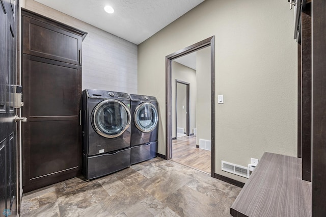 washroom with washing machine and clothes dryer, light stone finish flooring, baseboards, and a textured ceiling