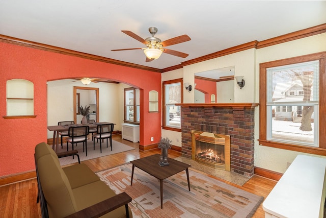 living room with crown molding, a fireplace, ceiling fan, and light wood-type flooring