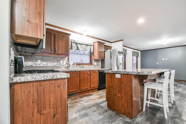 kitchen with sink, a center island, ornamental molding, and stainless steel refrigerator