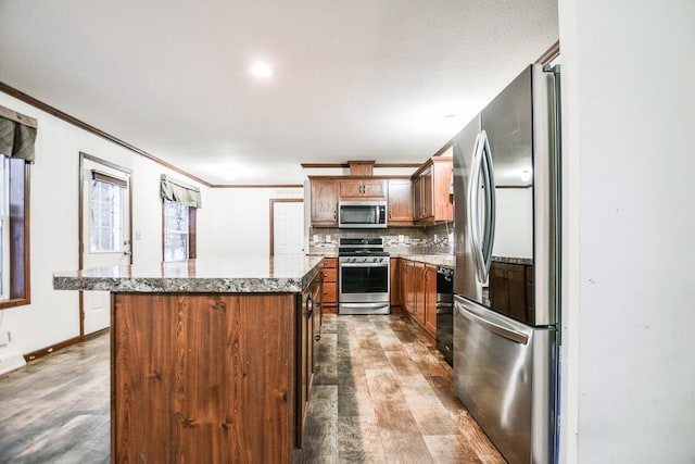 kitchen featuring appliances with stainless steel finishes, a kitchen island, light hardwood / wood-style flooring, backsplash, and light stone counters