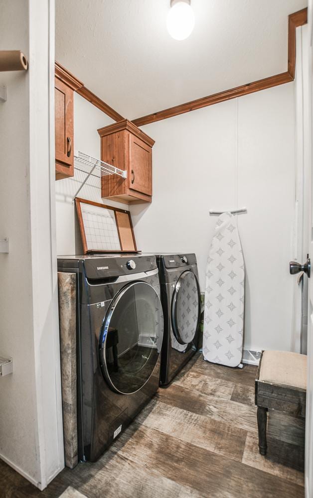 clothes washing area with washing machine and clothes dryer, crown molding, cabinets, and dark hardwood / wood-style flooring