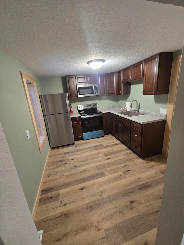 kitchen with a textured ceiling, appliances with stainless steel finishes, light hardwood / wood-style floors, sink, and dark brown cabinets