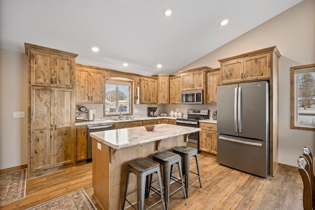 kitchen featuring vaulted ceiling, appliances with stainless steel finishes, a breakfast bar, a center island, and light hardwood / wood-style flooring