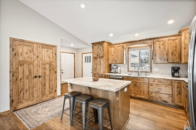 kitchen with vaulted ceiling, sink, a kitchen island, and light hardwood / wood-style flooring