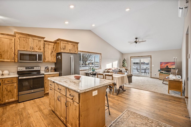 kitchen with vaulted ceiling, a kitchen island, appliances with stainless steel finishes, a kitchen bar, and light wood-type flooring