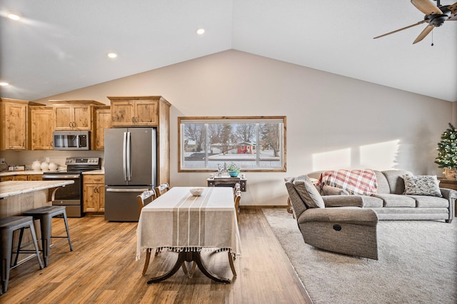 kitchen with stainless steel appliances, a breakfast bar, vaulted ceiling, and light hardwood / wood-style flooring