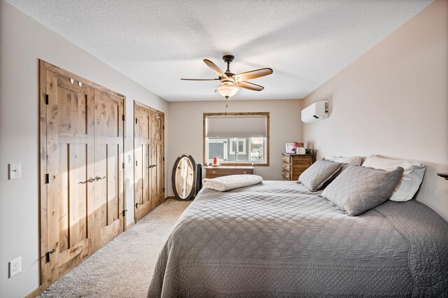 bedroom featuring ceiling fan, a wall unit AC, a textured ceiling, light carpet, and multiple closets