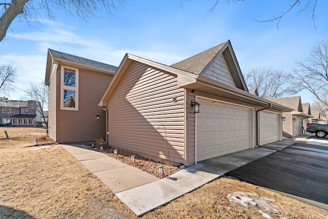 view of side of home featuring a garage, a shingled roof, and aphalt driveway