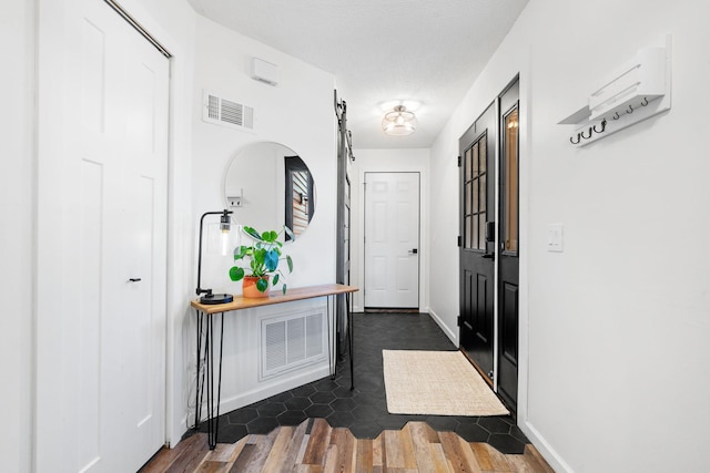 hall with dark wood-style flooring, visible vents, baseboards, and a barn door