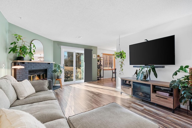 living area featuring a brick fireplace, a textured ceiling, baseboards, and wood finished floors