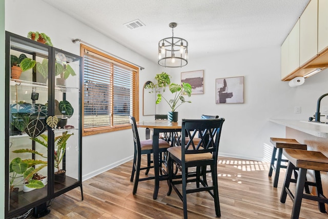 dining space with baseboards, visible vents, a textured ceiling, light wood-type flooring, and a notable chandelier