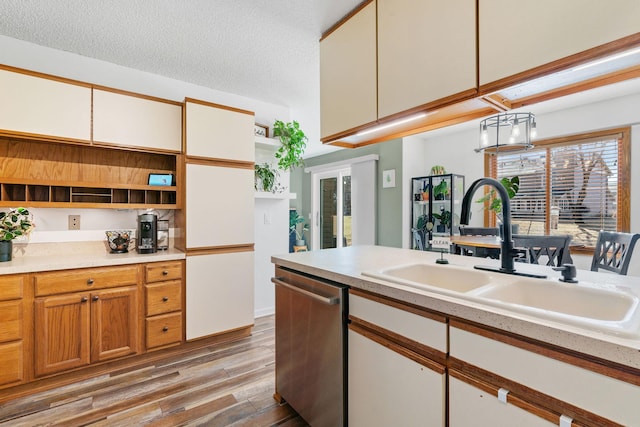 kitchen with light wood finished floors, open shelves, light countertops, stainless steel dishwasher, and a sink