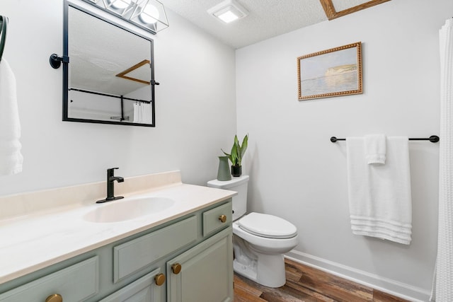 bathroom featuring toilet, a textured ceiling, vanity, wood finished floors, and baseboards