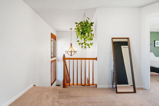 hallway featuring baseboards, an inviting chandelier, carpet, a textured ceiling, and an upstairs landing