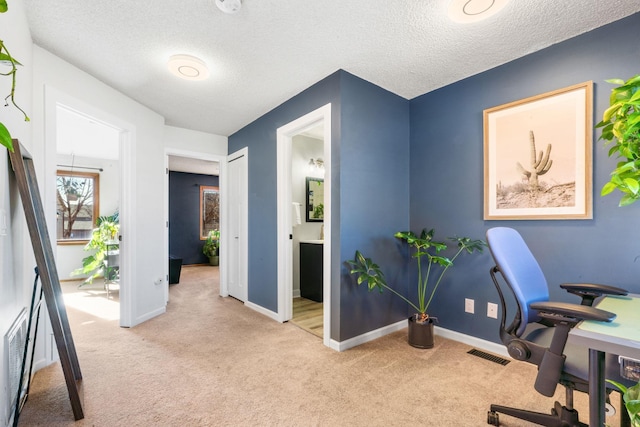 home office featuring baseboards, a textured ceiling, visible vents, and light colored carpet