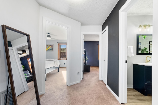 hallway with light carpet, a sink, a textured ceiling, and baseboards