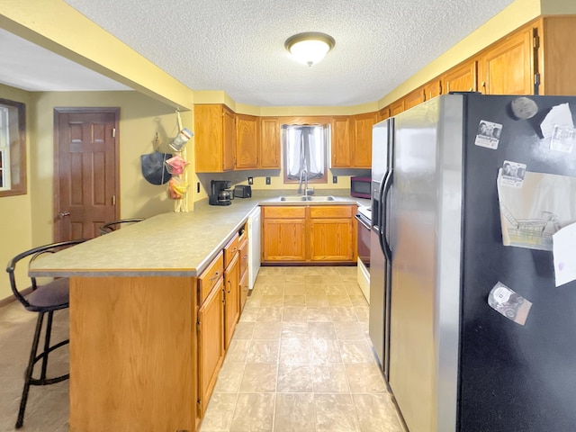 kitchen featuring stainless steel refrigerator with ice dispenser, sink, white dishwasher, a kitchen breakfast bar, and a textured ceiling