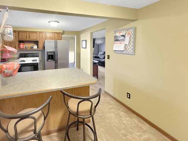 kitchen featuring electric range oven, hanging light fixtures, stainless steel fridge with ice dispenser, kitchen peninsula, and a breakfast bar area