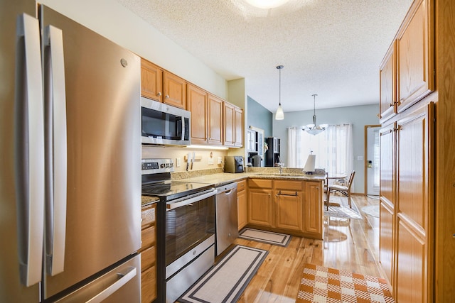 kitchen with pendant lighting, kitchen peninsula, light wood-type flooring, stainless steel appliances, and a textured ceiling