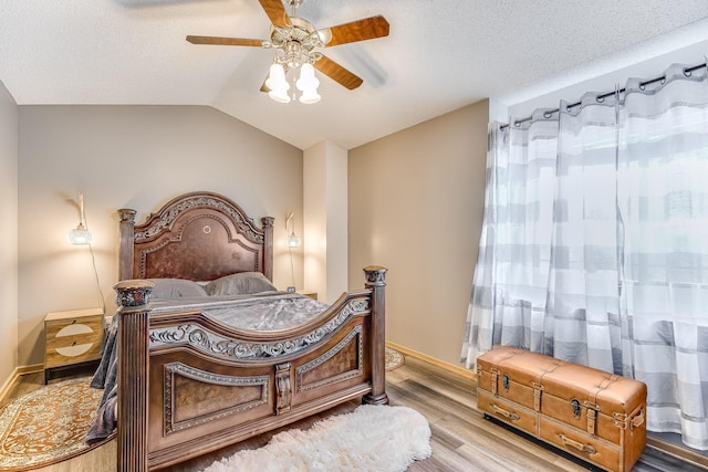 bedroom with ceiling fan, vaulted ceiling, a textured ceiling, and light hardwood / wood-style flooring