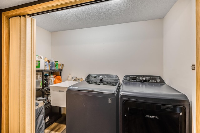 clothes washing area with washing machine and dryer, a textured ceiling, hardwood / wood-style flooring, and sink