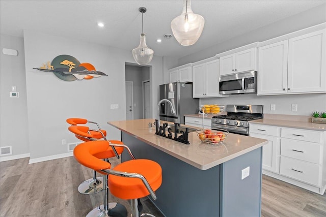 kitchen with a breakfast bar area, light countertops, appliances with stainless steel finishes, white cabinetry, and an island with sink