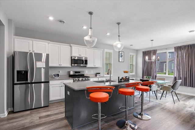 kitchen with a center island with sink, appliances with stainless steel finishes, hanging light fixtures, white cabinetry, and a sink