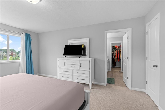 bedroom featuring light carpet, a textured ceiling, a walk in closet, and baseboards