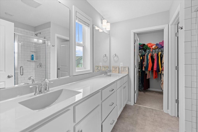 bathroom with a sink, a spacious closet, a shower stall, and double vanity