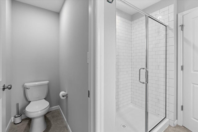 bathroom with a shower stall, toilet, and baseboards