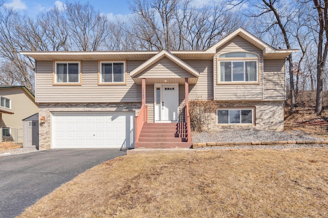 bi-level home with aphalt driveway, a garage, and brick siding