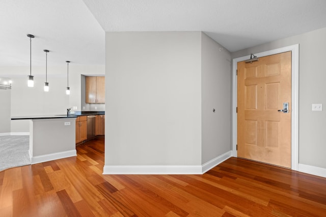 interior space featuring hardwood / wood-style floors, sink, hanging light fixtures, kitchen peninsula, and stainless steel dishwasher