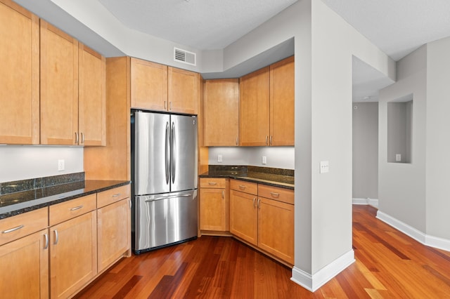 kitchen featuring dark stone counters, dark hardwood / wood-style floors, and stainless steel fridge