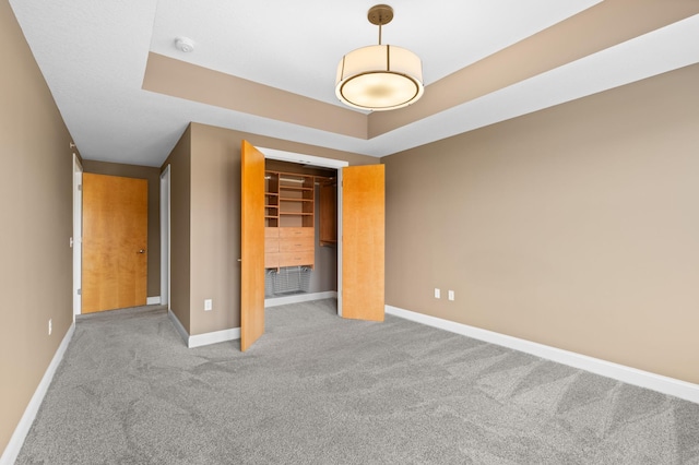 unfurnished bedroom featuring a tray ceiling, a closet, and light carpet