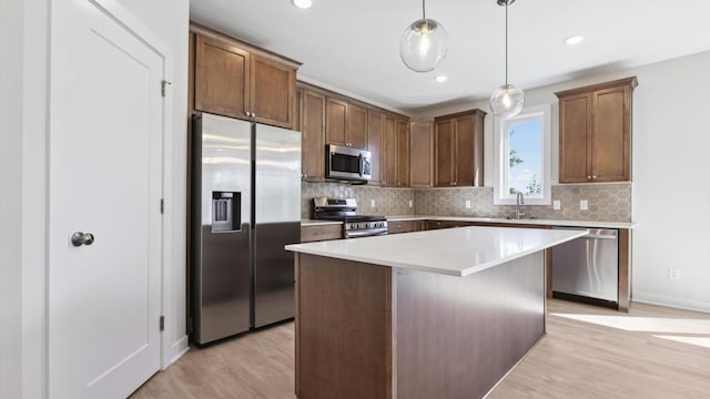 kitchen with hanging light fixtures, appliances with stainless steel finishes, sink, light wood-type flooring, and a center island