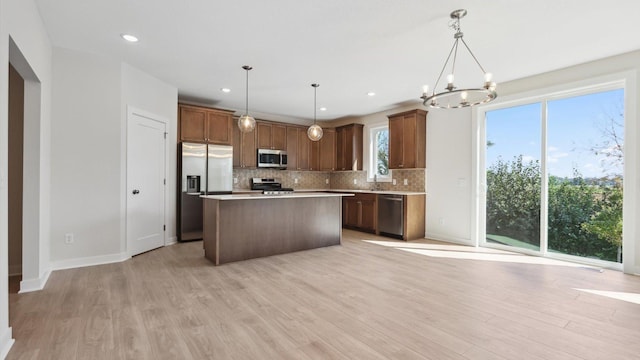 kitchen featuring hanging light fixtures, light wood-type flooring, a kitchen island, backsplash, and stainless steel appliances