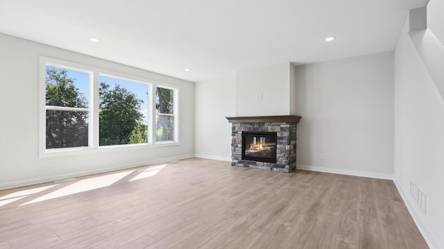 unfurnished living room featuring a stone fireplace and light hardwood / wood-style flooring