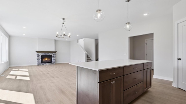 kitchen with a center island, a stone fireplace, light hardwood / wood-style floors, hanging light fixtures, and dark brown cabinetry