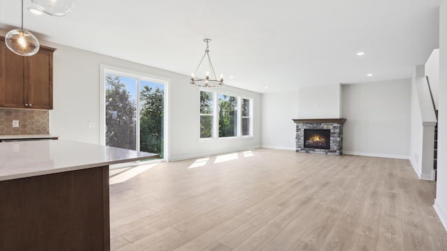 unfurnished living room featuring a chandelier, a stone fireplace, and light hardwood / wood-style floors