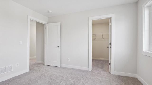 unfurnished bedroom featuring light colored carpet, a closet, and a walk in closet