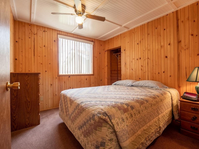 carpeted bedroom featuring a spacious closet, ceiling fan, and wooden walls