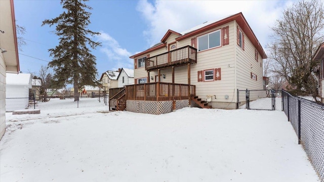 snow covered rear of property featuring a balcony and a wooden deck