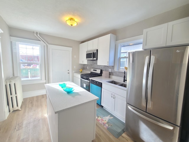 kitchen featuring radiator, a center island, white cabinetry, stainless steel appliances, and sink