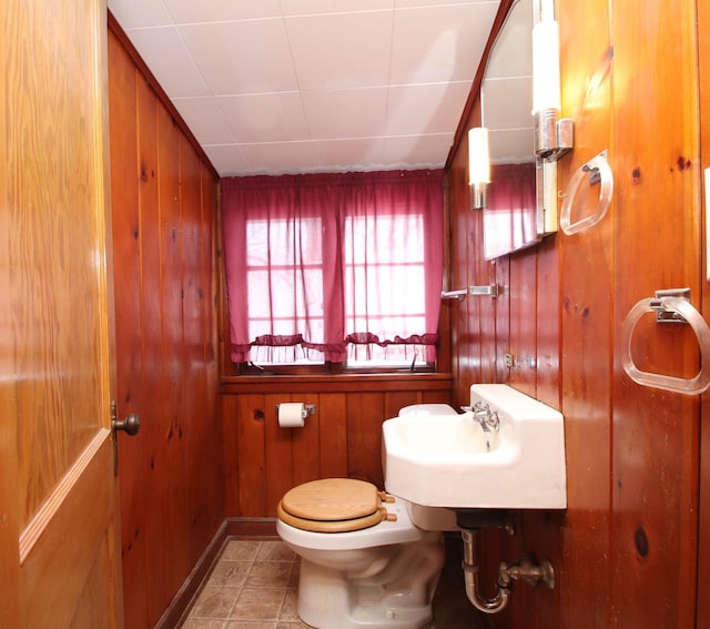 bathroom with toilet, tile patterned flooring, sink, and wood walls