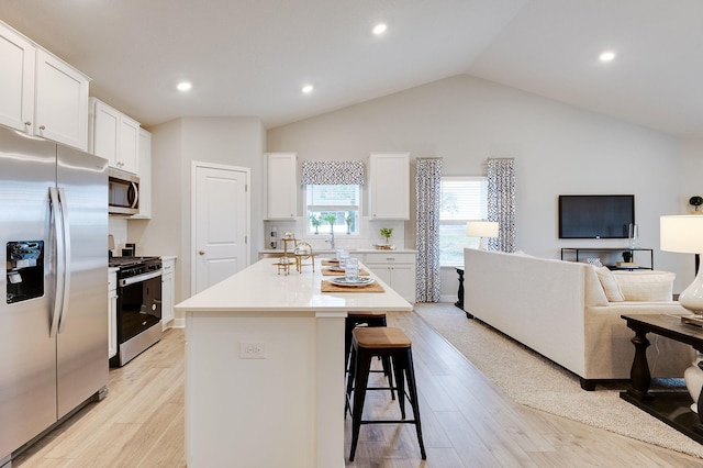 kitchen with light hardwood / wood-style flooring, white cabinetry, a kitchen breakfast bar, stainless steel appliances, and an island with sink