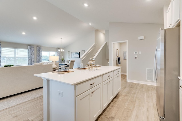 kitchen with lofted ceiling, stainless steel refrigerator, white cabinets, and a center island