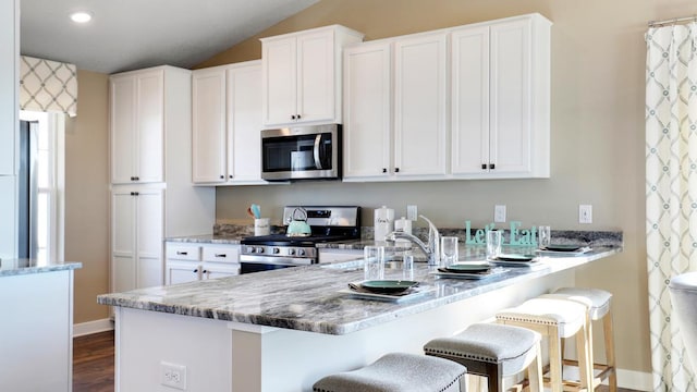 kitchen with a kitchen breakfast bar, appliances with stainless steel finishes, dark wood-type flooring, white cabinetry, and light stone counters