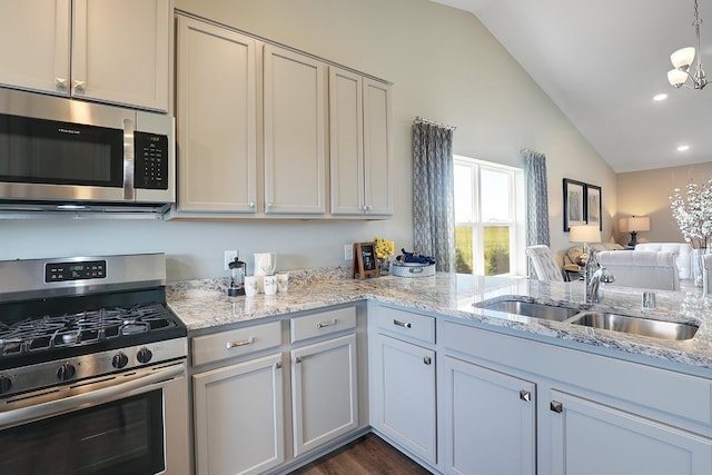 kitchen featuring appliances with stainless steel finishes, sink, a chandelier, vaulted ceiling, and light stone counters