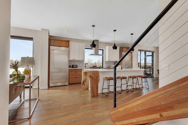 kitchen featuring pendant lighting, white cabinets, a kitchen island, stainless steel built in fridge, and backsplash